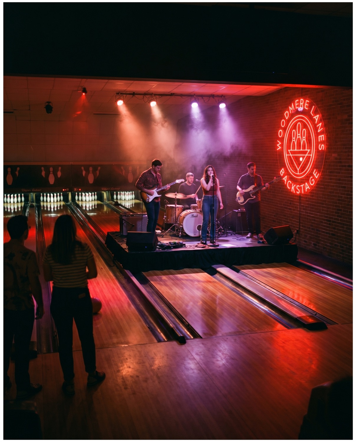 A live band playing on a stage over the lanes under red and purple light